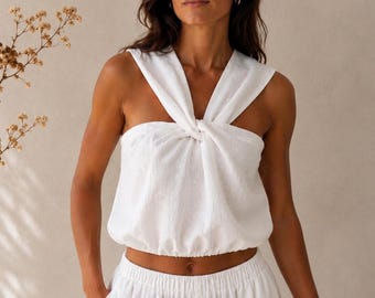 May include: A white sleeveless top featuring a twisted knot detail at the center of the chest, wide shoulder straps, and a gathered elasticized hemline, paired with matching white trousers that have an elastic waistband and side pockets.