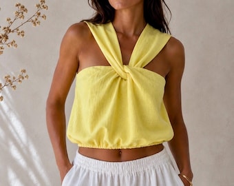 May include: A bright yellow sleeveless top featuring a knotted front detail and a gathered elasticized hem, paired with white shorts that have an elastic waistband and side pockets. The top has wide shoulder straps that cross at the center chest.