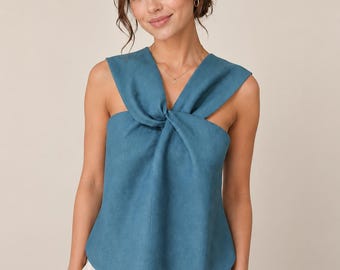 May include: A teal blue sleeveless top with a knotted front detail. The top has a V-neckline and cut-out shoulders. The model is wearing white pants. The top is made of a soft, textured fabric.