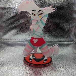 May include: A pink and white anime character figurine with a red heart on her skirt. She is tied up with blue rope and is kneeling on a red base with black horns.