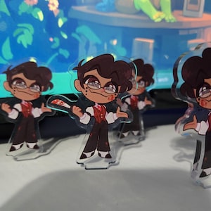 May include: A clear acrylic standee featuring a cartoon character with dark hair and glasses, wearing a red vest over a white shirt and dark trousers. The character holds a white knife with red spots and has red marks on their face and clothing.