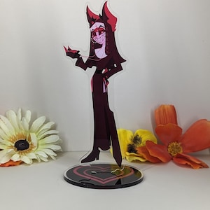 Puede incluir: Una figura de pie de acr&iacute;lico de un personaje de dibujos animados con cuernos, que lleva un vestido negro y est&aacute; de pie sobre una base con un coraz&oacute;n rojo.