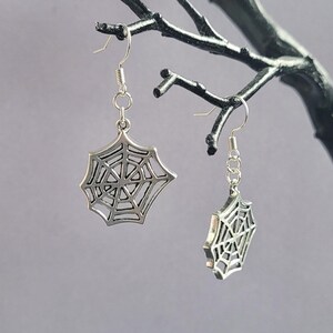 May include: A pair of silver spiderweb dangle earrings. The earrings are made of metal and have a delicate spiderweb design.