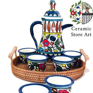 Può includere: Un set di sei tazze in ceramica colorate e una caraffa abbinata con motivi floreali, disposte su un vassoio intrecciato. Le tazze e la caraffa presentano motivi floreali blu, rossi, gialli e verdi. Il vassoio è fatto di vimini intrecciato.