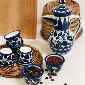 May include: A set of blue and white ceramic coffee cups and a matching jug with a floral design. The cups are filled with coffee beans and coffee grounds.