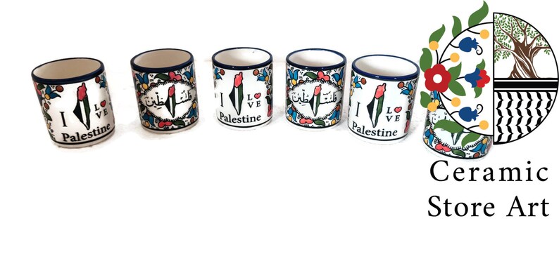 May include: Five ceramic mugs with a white background and blue trim. Each mug features a colorful design of the Palestinian flag and the words "I Love Palestine". The mugs are arranged in a row on a white background. The image also includes a logo for "Ceramic Store Art" with a stylized olive branch and floral design.
