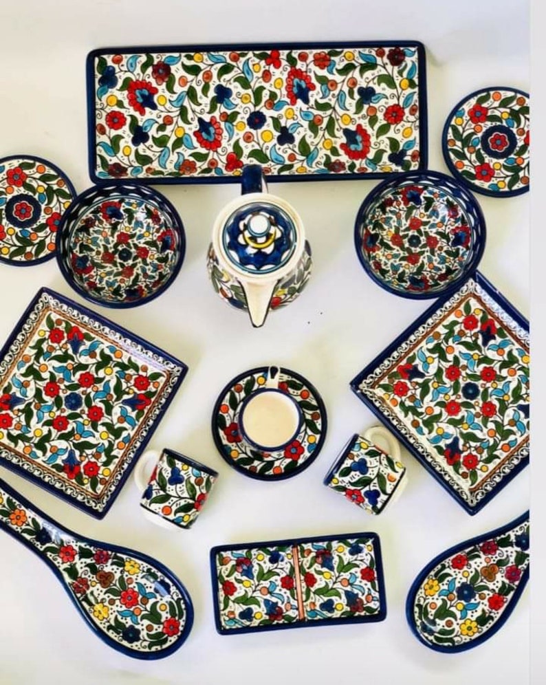 Może przedstawiać: Zestaw kolorowych ceramicznych naczyń z kwiatowymi wzorami w odcieniach niebieskiego, czerwonego, ż&oacute;łtego i zielonego. Zestaw zawiera talerze, miski, kubki, czajnik i łyżkę.