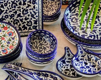 May include: A collection of blue and white ceramic dishes with floral patterns. The dishes include bowls, plates, and serving spoons. The dishes are arranged on a white surface with a wooden tray in the background.