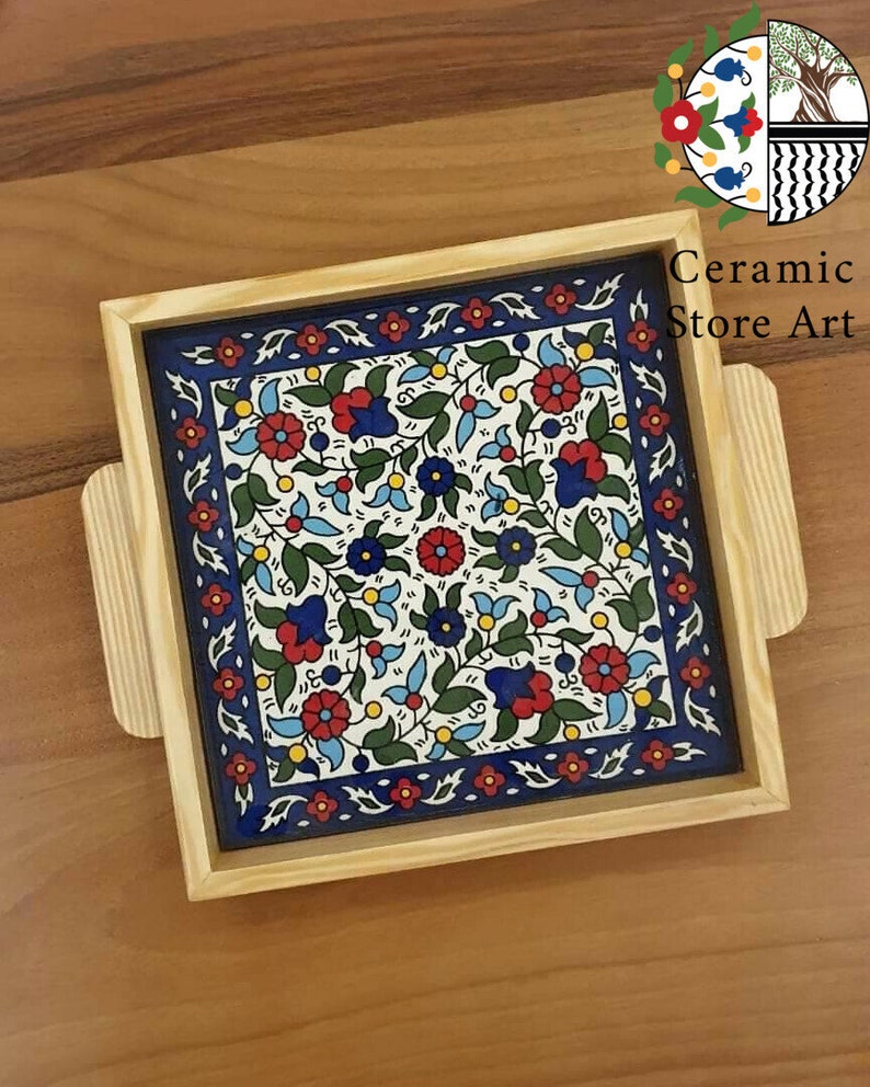 Puede incluir: Una bandeja de madera con una baldosa de cer&aacute;mica azul y blanca insertada. La baldosa presenta un patr&oacute;n floral con acentos rojos, azules, verdes y amarillos. La bandeja tiene dos asas a los lados.