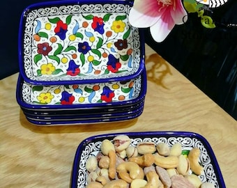 May include: A set of four blue and white ceramic rectangular dishes with a floral pattern. The dishes are stacked on top of each other. The top dish is filled with a variety of nuts, including cashews, almonds, and pistachios.