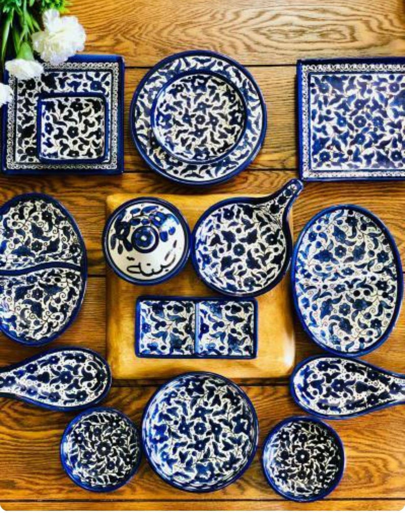 Może przedstawiać: Kolekcja niebieskich i białych ceramicznych talerzy, misek i naczyń do serwowania z misternymi wzorami kwiatowymi. Naczynia są ułożone na drewnianej powierzchni.