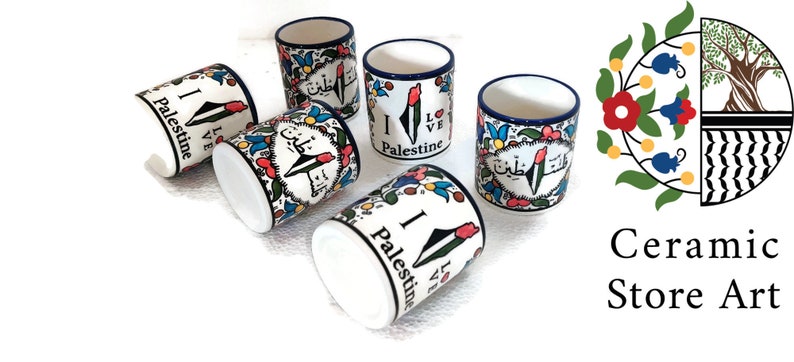 May include: Set of five white ceramic mugs with blue trim. Each mug features a colorful design with the words "I Love Palestine" in English and Arabic. The mugs are arranged in a circle on a white background.