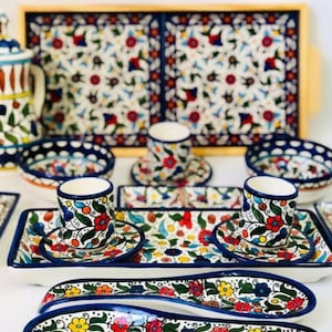 Może przedstawiać: Dwie białe ceramiczne łyżki do serwowania z niebieskimi i kwiatowymi wzorami. Łyżki znajdują się na białym tle z tacą i innymi naczyniami w tle.