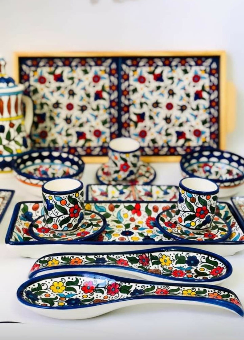 Może przedstawiać: Dwie białe ceramiczne łyżki do serwowania z niebieskimi i kwiatowymi wzorami. Łyżki znajdują się na białym tle z tacą i innymi naczyniami w tle.