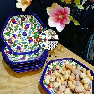 Puede incluir: Un juego de seis cuencos hexagonales de cerámica con un borde azul y un patrón floral colorido. Los cuencos están apilados uno encima del otro. Un solo cuenco está lleno de frutos secos mixtos.