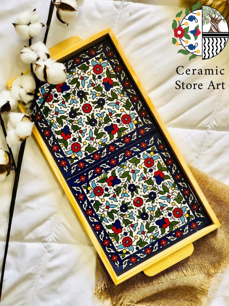Puede incluir: Una bandeja de servir de madera con dos azulejos de cer&aacute;mica extra&iacute;bles. Los azulejos presentan un patr&oacute;n floral colorido en tonos de azul, rojo, verde y blanco. La bandeja tiene un acabado de madera natural y dos asas.