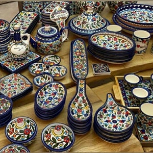 Może przedstawiać: Kolekcja kolorowych ceramicznych naczyń, misek, kubk&oacute;w i łyżek do serwowania z kwiatowymi wzorami. Naczynia są ułożone w stosy i rozmieszczone na drewnianej powierzchni. Niekt&oacute;re naczynia mają niebieskie i białe kwiatowe wzory, podczas gdy inne mają czerwone, ż&oacute;łte i zielone kwiatowe wzory.