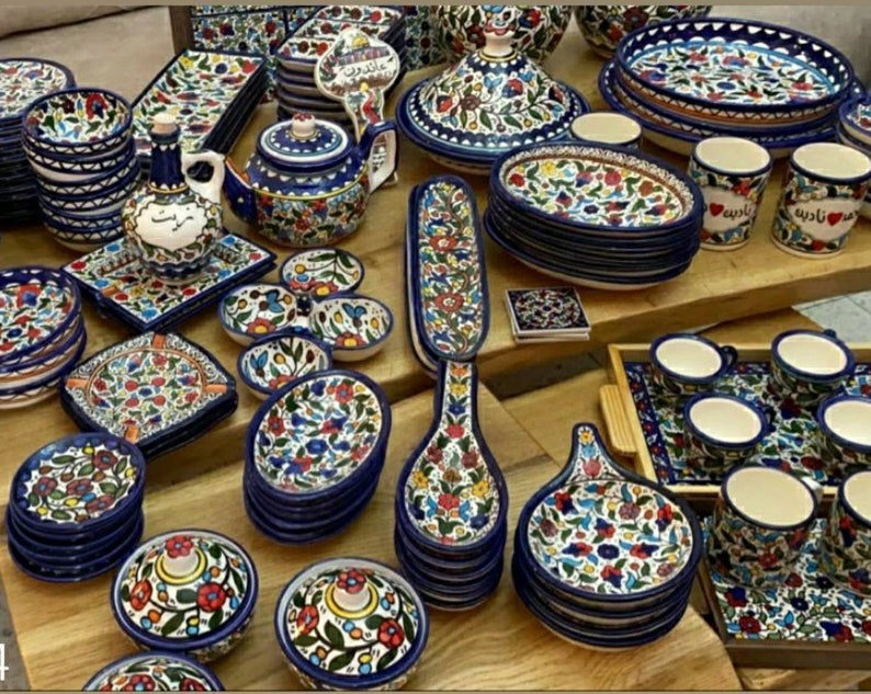 Może przedstawiać: Kolekcja kolorowych ceramicznych naczyń, misek, kubk&oacute;w i łyżek do serwowania z kwiatowymi wzorami. Naczynia są ułożone w stosy i rozmieszczone na drewnianej powierzchni. Niekt&oacute;re naczynia mają niebieskie i białe kwiatowe wzory, podczas gdy inne mają czerwone, ż&oacute;łte i zielone kwiatowe wzory.