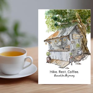 May include: Watercolor illustration of a rustic coffee shop under a tree, with the word "COFFEE" on a sign. The image includes the text "Hike. Rest. Coffee. Brewed for the journey." A white teacup and saucer are in the foreground.