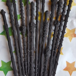 May include: A collection of 15 black wooden wands with intricate details. The wands are arranged in a fan shape on a white background with yellow stars.