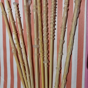 May include: A collection of ten wooden wands with clear glue applied to the tips. The wands are all different lengths and have various designs.