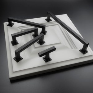 May include: A set of five black cabinet pulls and knobs in various sizes and styles. The pulls and knobs are displayed on a white surface.