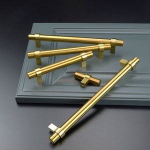 May include: Five gold cabinet pulls, including a single knob, on a gray surface. The pulls are all made of metal and have a polished finish.