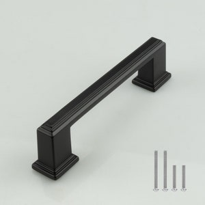 May include: Black cabinet hardware pull with a rectangular shape and a slightly raised edge. The pull is approximately 3 inches long. The image also shows four screws.
