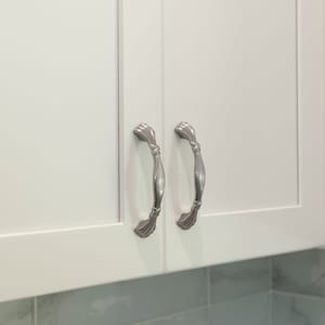 May include: Two silver cabinet pulls with a decorative design. The pulls are mounted on white cabinet doors.