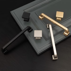 May include: Four cabinet hardware pulls in different finishes: black, gold, silver, and brushed nickel. The pulls are arranged on a dark gray surface.