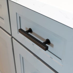 May include: A black cabinet door with a black rectangular drawer pull. The cabinet is painted a light blue color.
