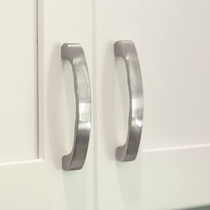 May include: Two silver cabinet pulls with a curved design. The pulls are mounted on white cabinet doors.