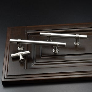 May include: Three silver cabinet pulls, two are long and rectangular with rounded ends and one is a smaller T-shaped pull.