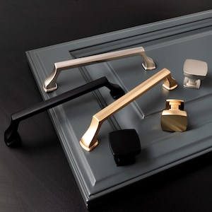 May include: Four cabinet pulls in different finishes: brushed nickel, black, gold, and black. The pulls are all the same style, with a rectangular shape and a slightly curved handle.