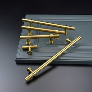 May include: A set of five gold cabinet pulls in various sizes and styles. The pulls are made of metal and have a polished finish.