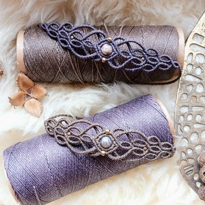 Peut inclure: Deux bobines de cordon avec des bracelets en macramé enroulés autour. Les bracelets sont faits de cordon brun et présentent une perle de pierre rose clair au centre. Les bobines sont brunes et violettes.