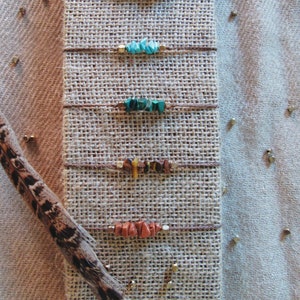 May include: Five different bracelets with various colored stones and beads on a burlap background. The bracelets are made with brown string and feature different colored stones, including white, turquoise, green, brown, and orange.