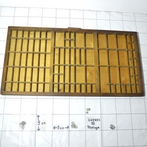 Può includere: Un vassoio da tipografia vintage in legno con numerosi piccoli scomparti. Il vassoio ha una cornice marrone scuro e un interno marrone chiaro. Le dimensioni sono di circa 9 cm per 9 cm. È visibile anche il testo "LOTSEL 11 Vintage".