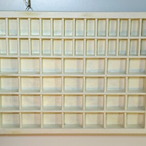 May include: A white wooden display case with multiple small square compartments. The case has a simple design and is perfect for organizing and displaying small items.