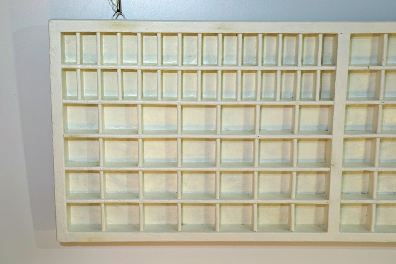 May include: A white wooden display case with multiple small square compartments. The case has a simple design and is perfect for organizing and displaying small items.