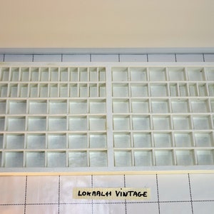 May include: White plastic storage box with multiple compartments. The box is empty and has a label that says "LOKAALI VINTAGE".