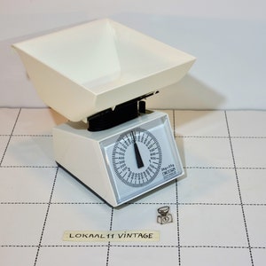 May include: White vintage kitchen scale with a large bowl and a round dial. The dial has markings for grams and kilograms. The scale is on a white tiled surface.