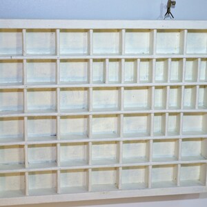May include: White wooden display case with multiple small square compartments. The case is empty.