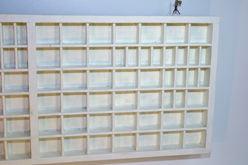 May include: White wooden display case with multiple small square compartments. The case is empty.