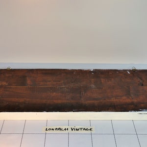 May include: The back of a wooden sign with a white painted frame. The sign has two brass hanging hooks and the text "LOKAALI VINTAGE" is written on a piece of tape on the bottom.