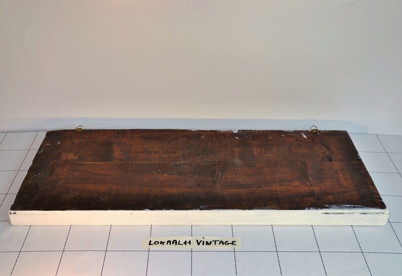 May include: The back of a wooden sign with a white painted frame. The sign has two brass hanging hooks and the text "LOKAALI VINTAGE" is written on a piece of tape on the bottom.