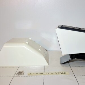 May include: Two white plastic bases for a vintage record player. The bases are different sizes and shapes. The larger base has a black top and a black stand.