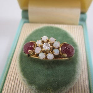 May include: A gold ring with a cluster of white opals and a single diamond in the center. The ring is flanked by two red ruby stones.