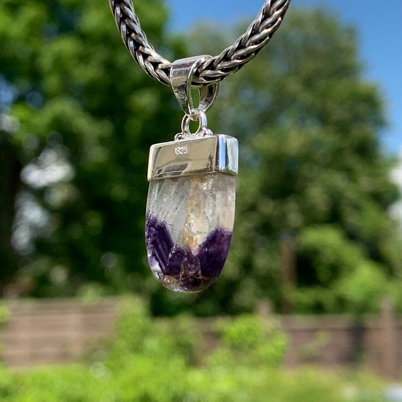 May include: A silver pendant with a clear crystal featuring purple and gold accents. The pendant is marked with "925" on the top.