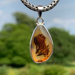 May include: A teardrop-shaped pendant with a brown and white agate stone set in sterling silver. The stone has a unique pattern of brown and white swirls.